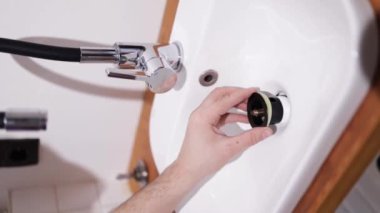 Tesisatçı lavabo atık tuzağını tamir ediyor. Bir adamın elleri banyodaki lavabonun altındaki tesisatı tamir ediyor. Oda servisi, el sanatları ve inşaat kavramı, dikey video.