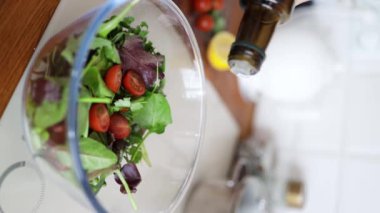 Mutfak konsepti, ev yapımı yemekler için hazırlama malzemeleri. Dikey çekim, yemek pişiren tanınmayan bir kadını vurdu. Salatayı içeride salata kasesine döktü. Sebzeler masada.