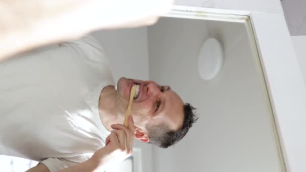 垂直录像 年轻人在浴室里刷牙 负责清洁口腔的人每天早上都在做牙科护理 白种人使用天然竹子生态刷 — 图库视频影像