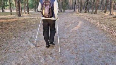 İskandinavya yürüyüş sopaları. Orman parkında gün batımında İskandinav kutuplarını tutan adam.