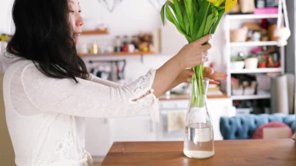アジアの若い女性がキッチンで花瓶にチューリップの花束を置く — ストック動画