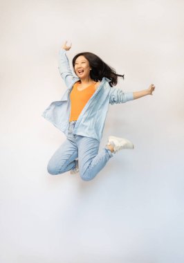 Beyaz arka plan stüdyosunda izole edilmiş, turuncu tişörtlü, neşeli ve mutlu Asyalı bir kadın..