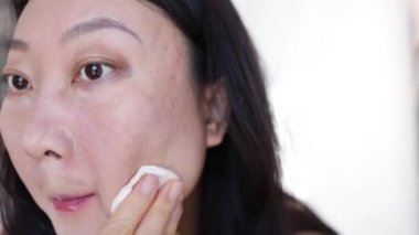 Asyalı kadın yanlışlıkla makyajı kaldırıyor yüzüne sürtünerek makyaj temizleme eğitimi alıyor temel rimelini pamuk yünüyle temizliyor ve yüz ifadeleri yapıyor.