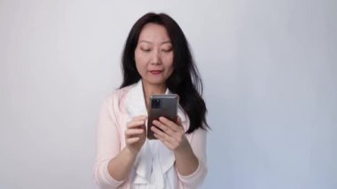 Mutlu Asyalı iş kadını elinde telefonla stüdyoda beyaz arka planda iyi haberler alıyor..