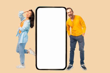 Sarı arka planda boş ekranı olan akıllı telefonlu mutlu bir çift. Model