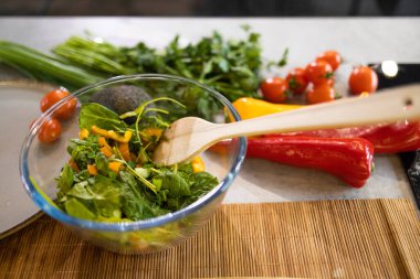 Kadın taze ve sağlıklı bir vejetaryen salatası hazırlıyor. Mutfakta bir sürü sebze var ve yeni bir tarif deniyor.