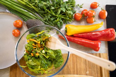 Kadın taze ve sağlıklı bir vejetaryen salatası hazırlıyor. Mutfakta bir sürü sebze var ve yeni bir tarif deniyor.