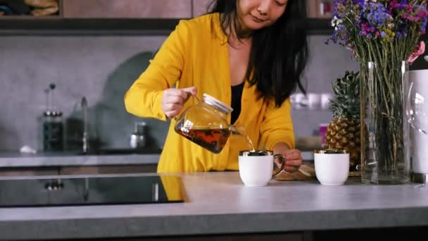 黄色いシャツの女性は 白いカップに紅茶を入れます ホスピタリティコンセプト ホステスはお茶にゲストを扱います — ストック動画