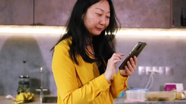Азиатка Отдыхает Стоя Кухне Провести Смартфон Выбрать Товары Интернете Сделать — стоковое видео