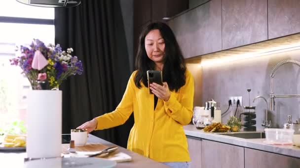 Asyalı Bir Kadın Mutfakta Dinleniyor Akıllı Telefon Internetten Mal Seçiyor — Stok video