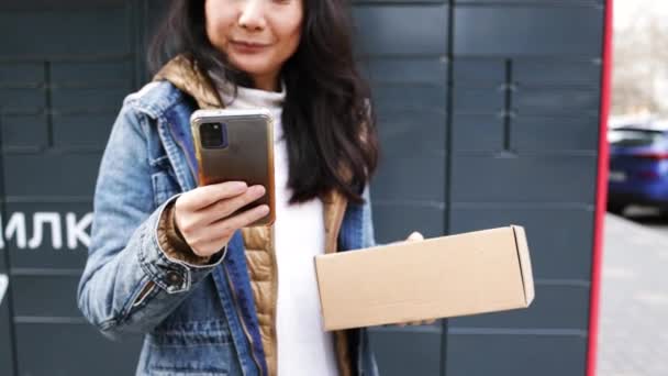 屋外でスマートフォンを使用した郵便端末機から小包を受け取る女性 小包の配達機械 メール配信とポストサービス オンラインショッピング Eコマースコンセプト — ストック動画