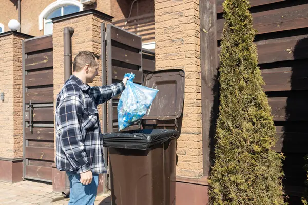 Man throwing out black eco-friendly recyclable trash bag in to big plastic green garbage container. Take out the trash.