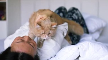 Asyalı bir kadın evde küçük bir kediyle sarılıp oynuyor. Çekici kadın yatağa uzanıyor, boş zamanlarını evdeki yatak odasında nazik bir şekilde evcil hayvanına sarılıp masaj yaparak geçiriyor..