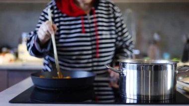 Modern mutfakta sebzeleri kızartma tavasında karıştıran kıdemli kadın..