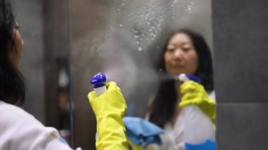 Bir kız banyoda ayna yıkıyor. Eller yukarı. Temizlik konsepti. Ev hanımı çalışıyor. Genç ve güzel bir kadın banyodaki aynayı temizliyor. Hizmetçi evi temizliyor..