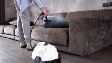 Ev temizliği. Bir adam kanepeyi ve mobilyaları buhar jeneratörüyle temizliyor. Dairenin temizlik servisi. Düz Los. Güçlü buhar basıncı.