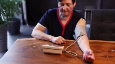 Yüksek tansiyonu olan ve aşırı kilolu yaşlı bir kadın evde arteryel kan basıncını ölçüyor. Sağlıklı bir konsept. bir tonometre ile nabız ve basınç kontrolü. 