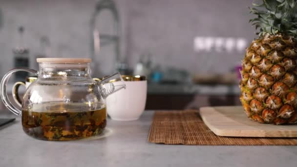 キッチンテーブルのガラスティーポットで緑茶を醸造する 新鮮なジャスミンの花でケトルに湯を注ぐ 水に花茶ジャスミンの花を作る — ストック動画