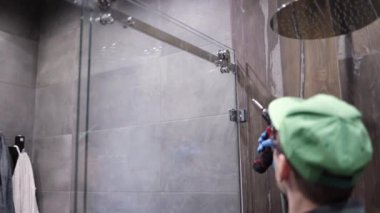 Üniformalı genç adam banyodaki duş kapısını tamir ediyor. Erkek bir tamirci duş kabinini tamir ediyor..
