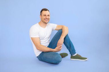 Yakışıklı genç sakallı adam mavi arka planda izole edilmiş kameraya gülümsüyor..