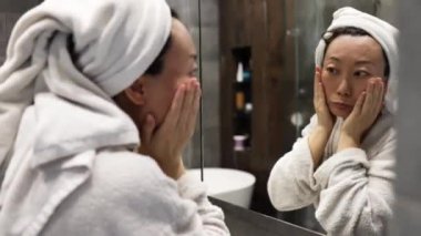 Aynaya bakan endişeli 40 'lı yaşlardaki Asyalı kadın, yüz kırışıklığı sorunu yüzünden stresli, sinirli kadın, banyodaki kuru hassas cilt bakımı konsepti yüzünden depresif..