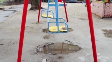 Yağmurdan sonra boş oyun alanı. Salıncak yağmur damlaları içinde ıslanmış. Yaz veya bahar yağmurlu bir gün. İnsan yok. Çocuk yok.