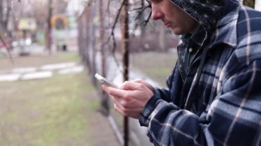 Eski çitlerin yanında cep telefonu kullanan üzgün genç bir adam. Yalnız yaşayan üzgün adam stresli, düşünceli, aile sorunları, stres, şiddet, depresyon konsepti..
