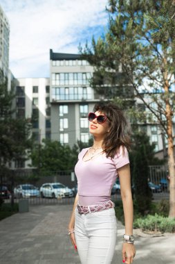 Siyah saçlı, sevimli, şık bir kadın. Gözlük takıyor ve şık kıyafetler giyiyor. Sokakta yürüyor..