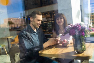 Açık havada kafe masasında otururken, cep telefonu kullanarak aşık çekici genç çift öğle yemeği.