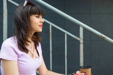 Merdiven başında oturan endişeli genç bir bayan şehirde cep telefonu sinyalini bekliyor..