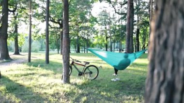 Kadın bisiklete biniyor, mavi hamakta dinleniyor, yaz ormanlarında dinleniyor. Hamakta, ağaçların arasında kamp alanında bisiklet süren biri. Günbatımında hamakta bisikletli bir kadın.