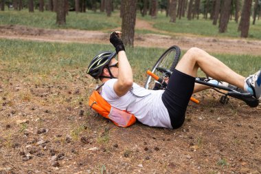 Yorgun bir bisikletçi yolda yere düştü. Spor ve eğlence konsepti. Bir adam parkta bisikletinden düştü. Bisiklet kazası. Bisikletli yolda uzanıyor ve bacağını tutuyor..