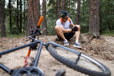 Yorgun bir bisikletçi yolda yere düştü. Spor ve eğlence konsepti. Bir adam parkta bisikletinden düştü. Bisiklet kazası. Bisikletli yolda uzanıyor ve bacağını tutuyor..
