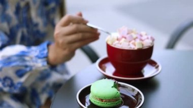 Bir kız çay kaşığıyla bir fincanda marşmelov karıştırıyor, yakın plan. Masanın üzerinde bir fincan kakao ve marşmelov var. Bir kızın eli bir çay kaşığı kakaoyu karıştırıyor.. 