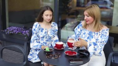Anne ve genç kız yaz terasında kafede ferahlatıcı içkiler içerler. Dişi çocuk, annesiyle şehirde vakit geçirmekten hoşlanıyor..