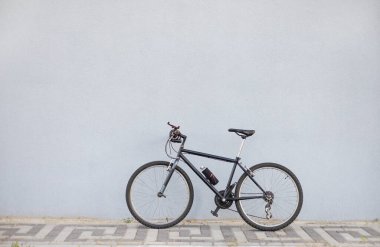 Fotokopi alanı olan gri bir duvara yaslanmış siyah bisiklet. Yan görünüm.