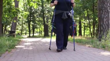 Şehir parkında yürüyüş direkleri olan kıdemli, aktif, beyaz bir kadın. Olgun bir fitness kadını doğada İskandinav yürüyüşü yapıyor. Yaşlı sporcu kadın İskandinav yürüyüşü yapıyor..