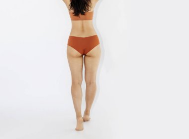 Şefkatli güzellik. Güzel gülümseyen Asyalı kadının uzun bir portresi. İç çamaşırlı, bej renkli stüdyo arka planında poz vermiş. Kadın vücudu kavramı, sağlık, spor, spa, reklam