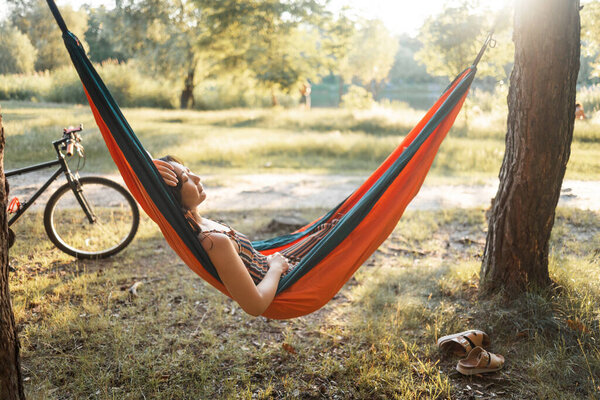 Dreaming woman relaxes and meditates in a hammock in the forest after riding a bike on a sunny day - wonderful weekend in nature.