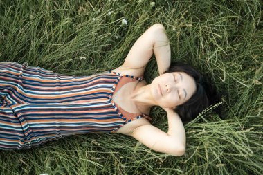 Güzellik Taze Romantik Asyalı Kız Açık Hava. Doğa. Bahar Günbatımı. Tarlada uzun siyah saçlı güzel bir manken. Çinli Kız Güneş Işığında Sahada Uzanıyor.