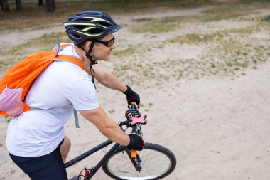 Bisiklet kıyafetleri, miğfer ve güneş gözlüğü takmış bisiklet yolunda bisiklet süren mutlu bir adamın portresi. Aktif sporcu imajı.