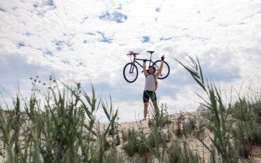 Dağ bisikletçisinin silueti gün batımında zaferin sembolü olarak bisikletini kaldırıyor. Kişisel motivasyon.