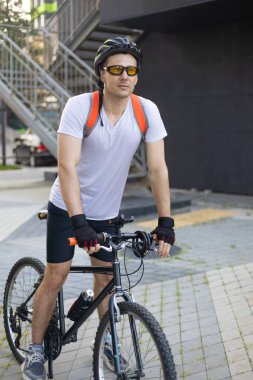 Şehir merkezinde bisiklet sürerken çekici bir adamın durması. Şehirde bisiklet sürerken gülümseyen yakışıklı bir sporcunun ön görüntüsü. İşe bisikletle gidip gelme kavramı.