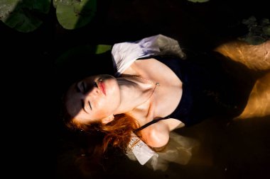 Güneşli bir günde gölün sularında uzun kızıl saçlı güzel bir kadın..