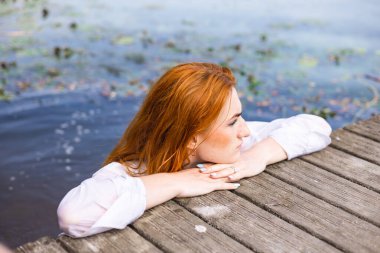 Güneşli bir günde gölün sularında uzun kızıl saçlı güzel bir kadın..