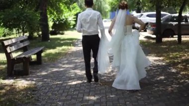 Gelin ve damat elbiseleriyle yürüyor, arka planda yürüyen çift görülüyor..