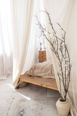 Yatak odasında parlak bir Scandi tarzı iç mekan. Bir gölgelik, keten bir yatak ve jüt bir halı. Tam boy pencereler. Dikey çekim. 