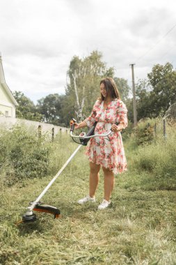 Beyaz kadın arka bahçesinde çim biçme makinesiyle çim biçiyor.