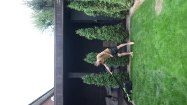 Arka bahçedeki çimleri elektrikli çim biçme makinesiyle biçen bir adamı yakından çek. Yavaş çekim.