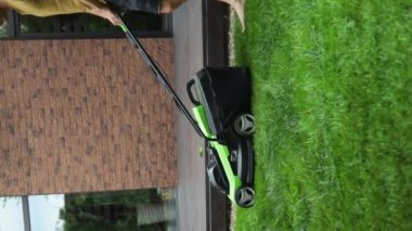 Arka bahçedeki çimleri elektrikli çim biçme makinesiyle biçen bir adamı yakından çek. Yavaş çekim.